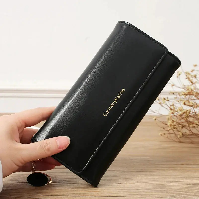 Black PU leather long wallet with fold design and gold logo lettering, held in hand with a small keychain.