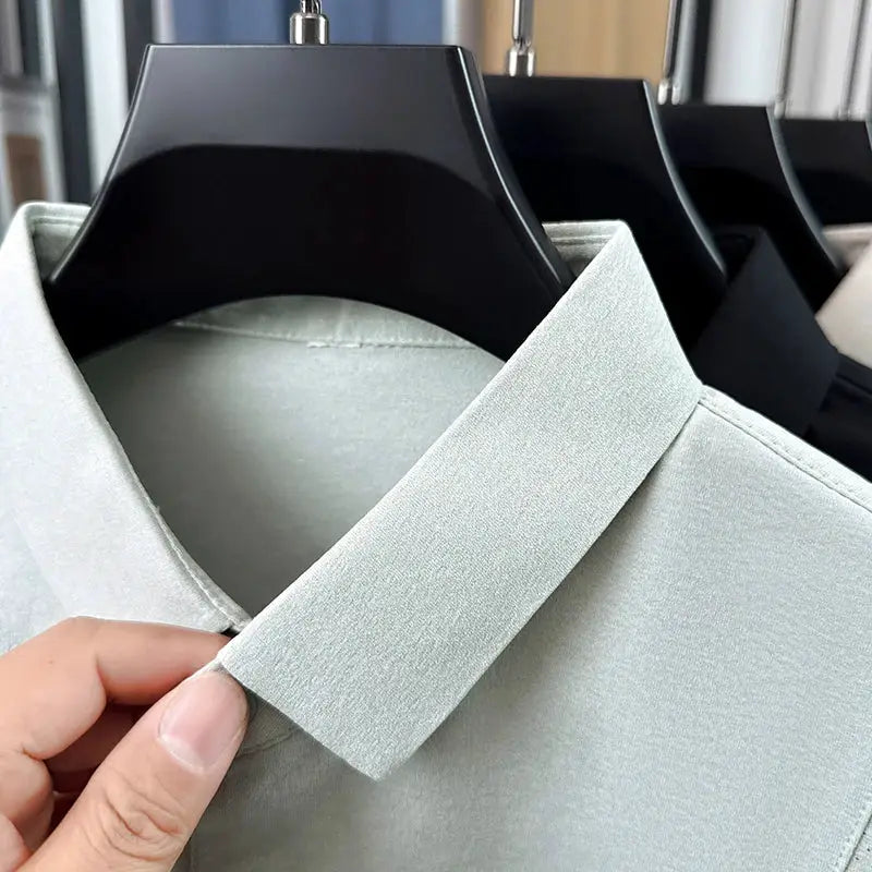 Three men's polo shirts on hangers; light gray polo in front with minimalist collar.