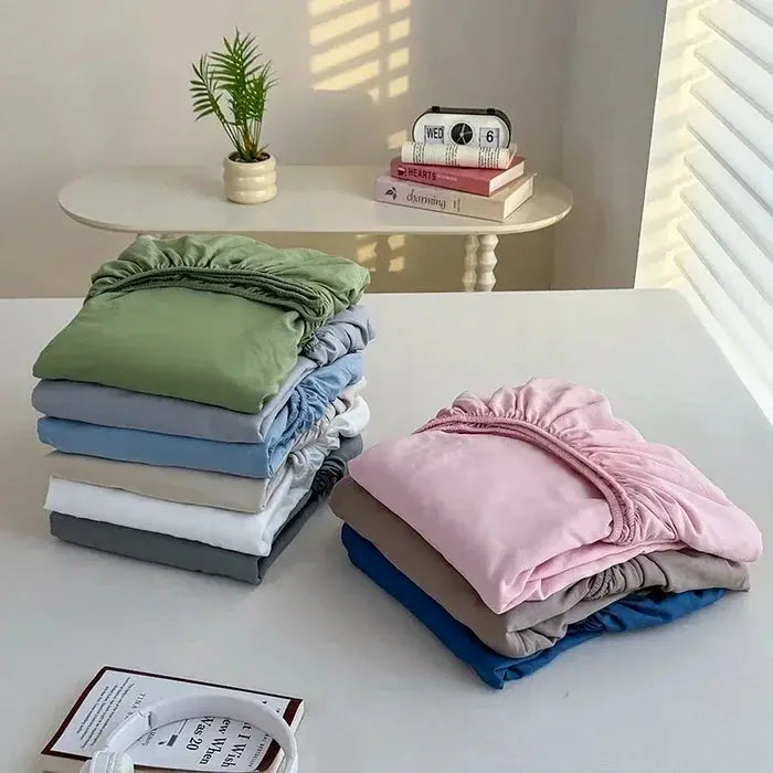 Washed fitted sheet set with elastic bands; assorted pastel-colored sheets folded in stacks on a white table.