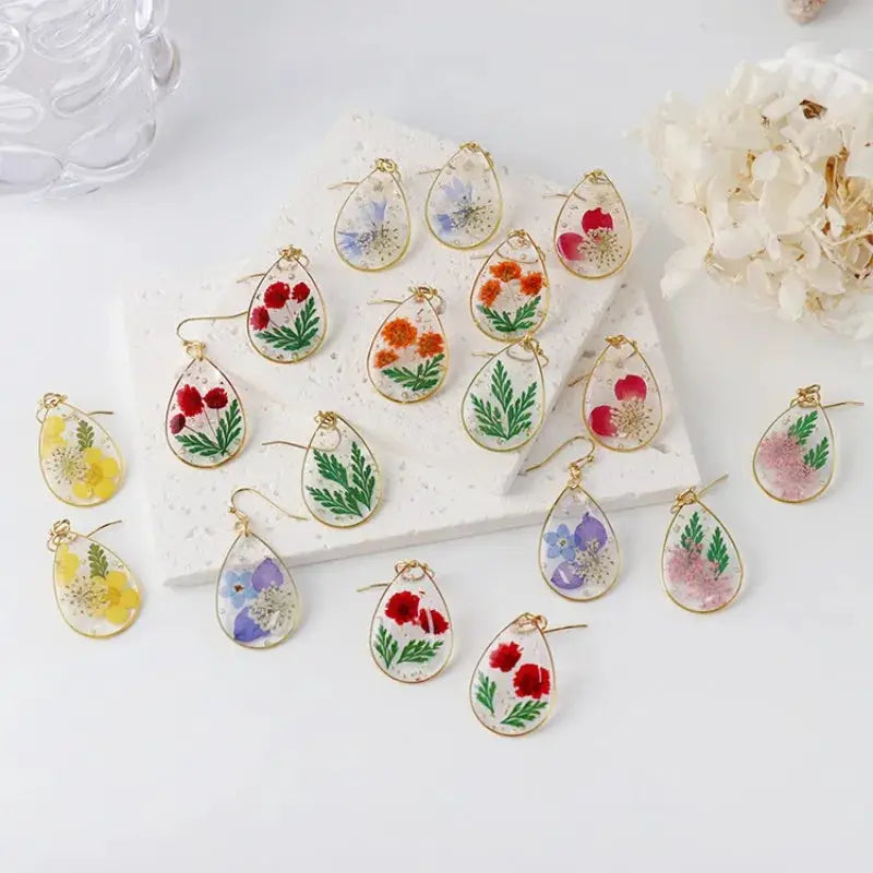 Teardrop epoxy resin flower earrings with pressed blooms in assorted colors, gold-tone frame.