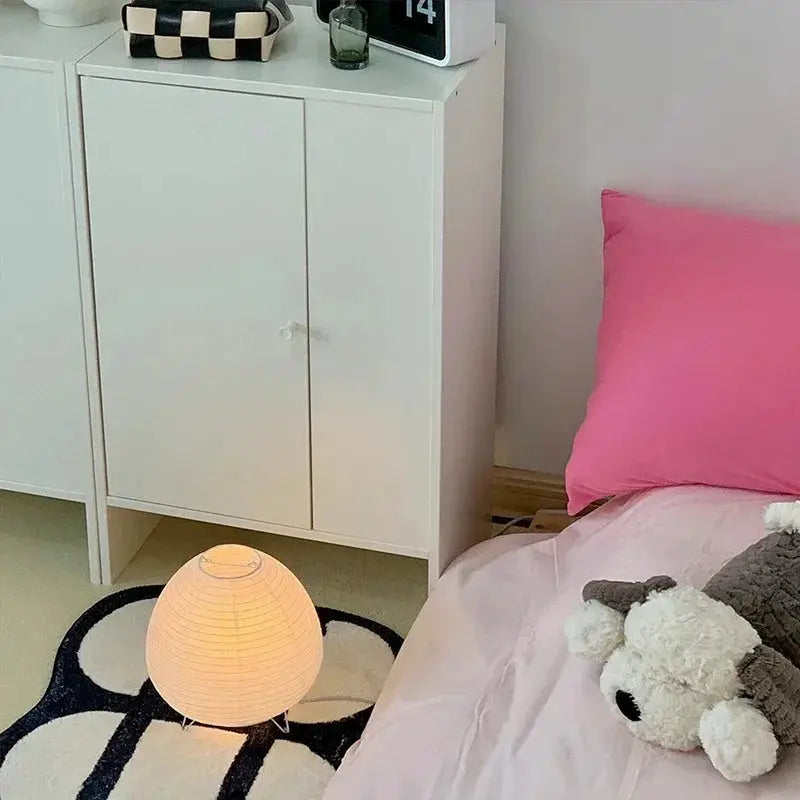 Japanese Lantern LED Table Lamp by Simples Market, warm rice-paper glow beside a white cabinet.