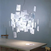 White paper chandelier with handwritten notes hanging from wires over a dining table in a minimal room