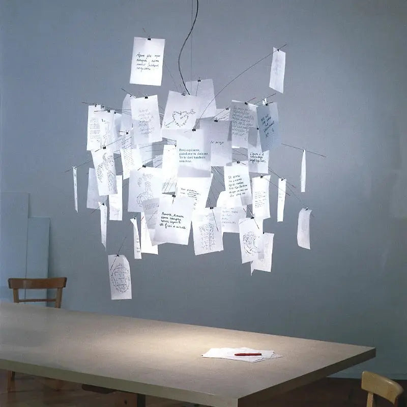 White paper chandelier with handwritten notes hanging from wires over a dining table in a minimal room
