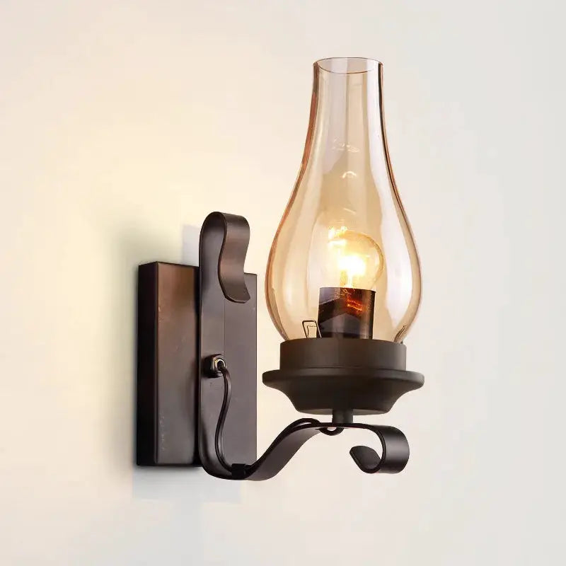 Wrought-iron wall lamp with clear glass lantern shade, black finish, industrial-style.