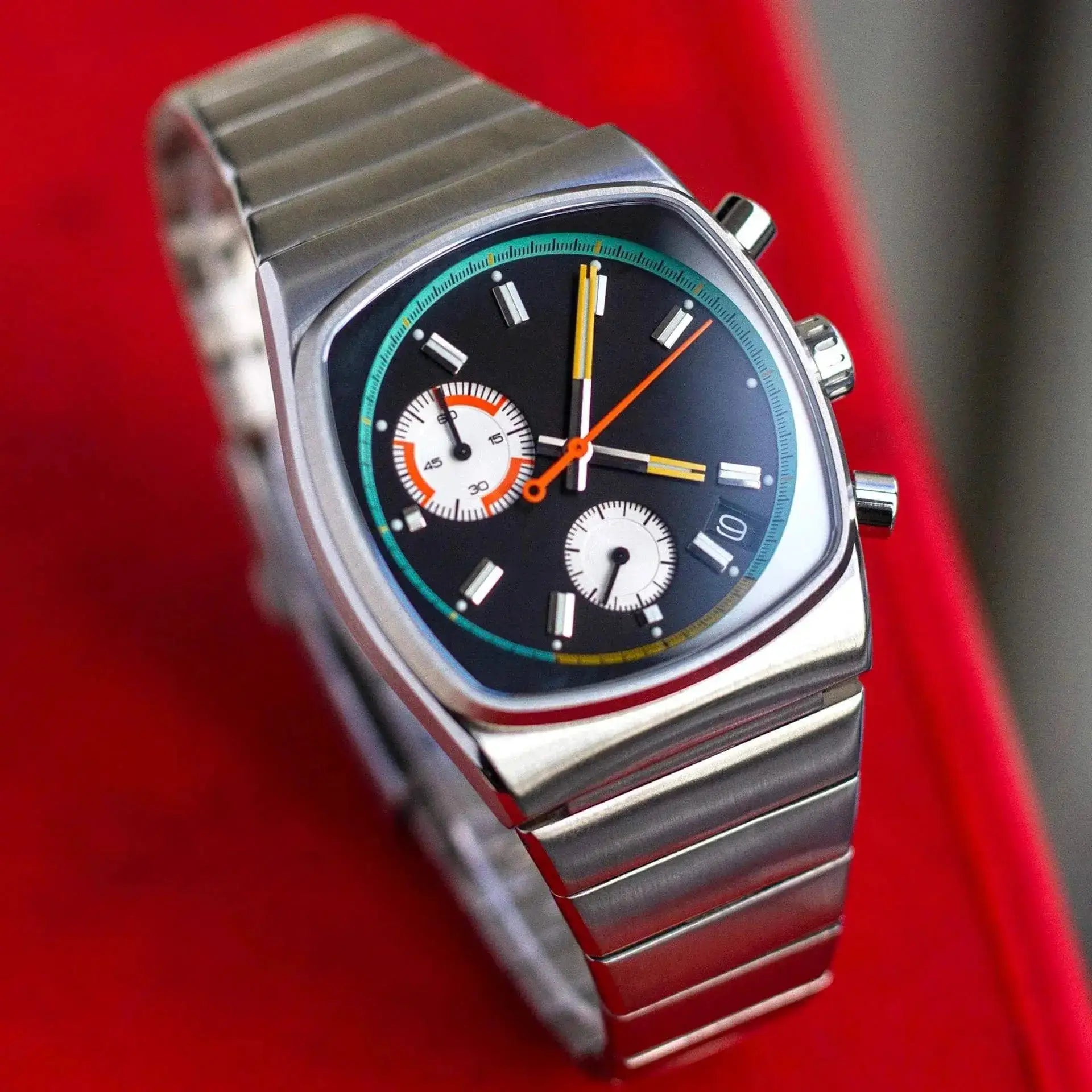 Square stainless steel men's watch with black dial, turquoise bezel, orange hands and chronograph subdials.