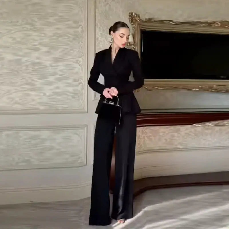 Black women's two-piece peplum jacket set with high-waisted wide-leg pants and a small black handbag