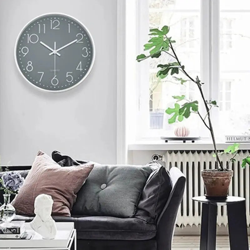 8-inch round wall clock with gray face, white numerals, and a silver bezel mounted on a white wall above a sofa.