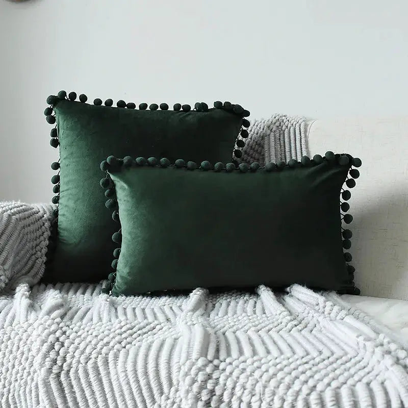 Velvet cushion covers by Simples Market; dark green plush with pom-pom fringe for sofa decor.