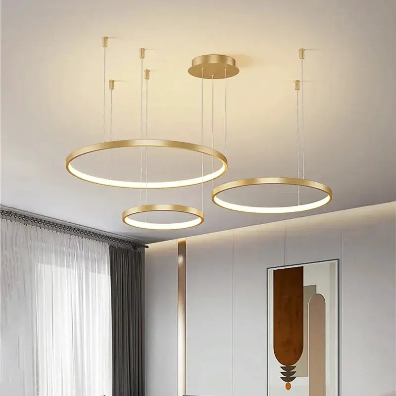 Minimalist three gold circular pendant lights with acrylic LED rings hanging over a living room.