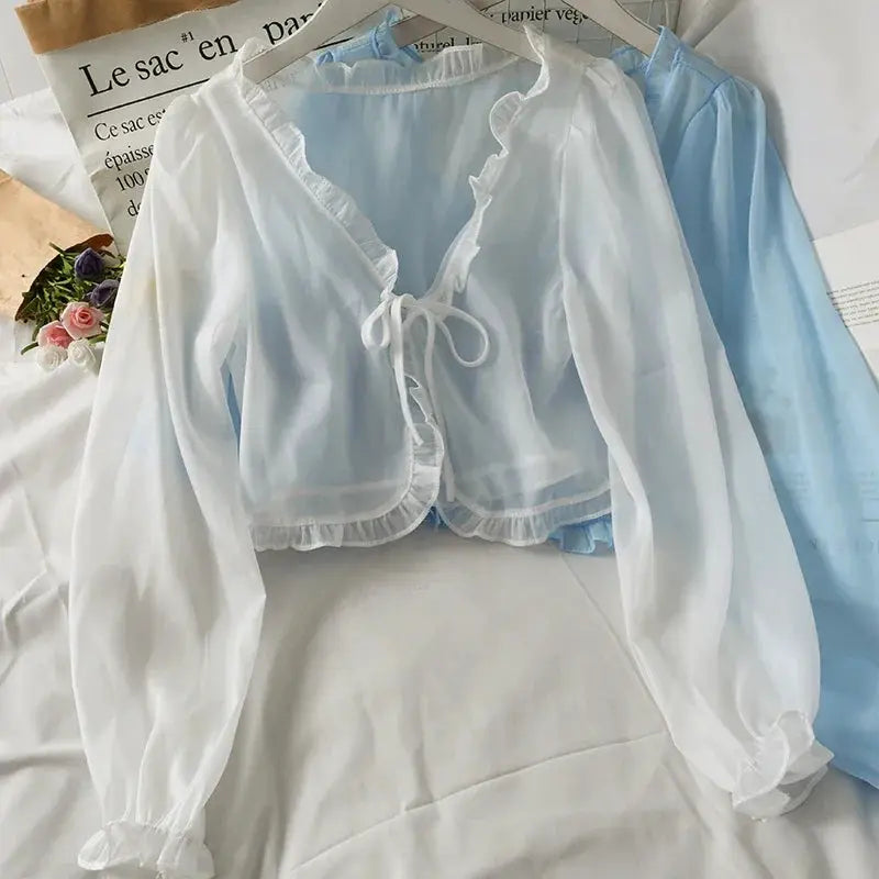 White sheer long-sleeve cardigan with lace-trimmed ruffles and front bow, layered over a light-blue blouse