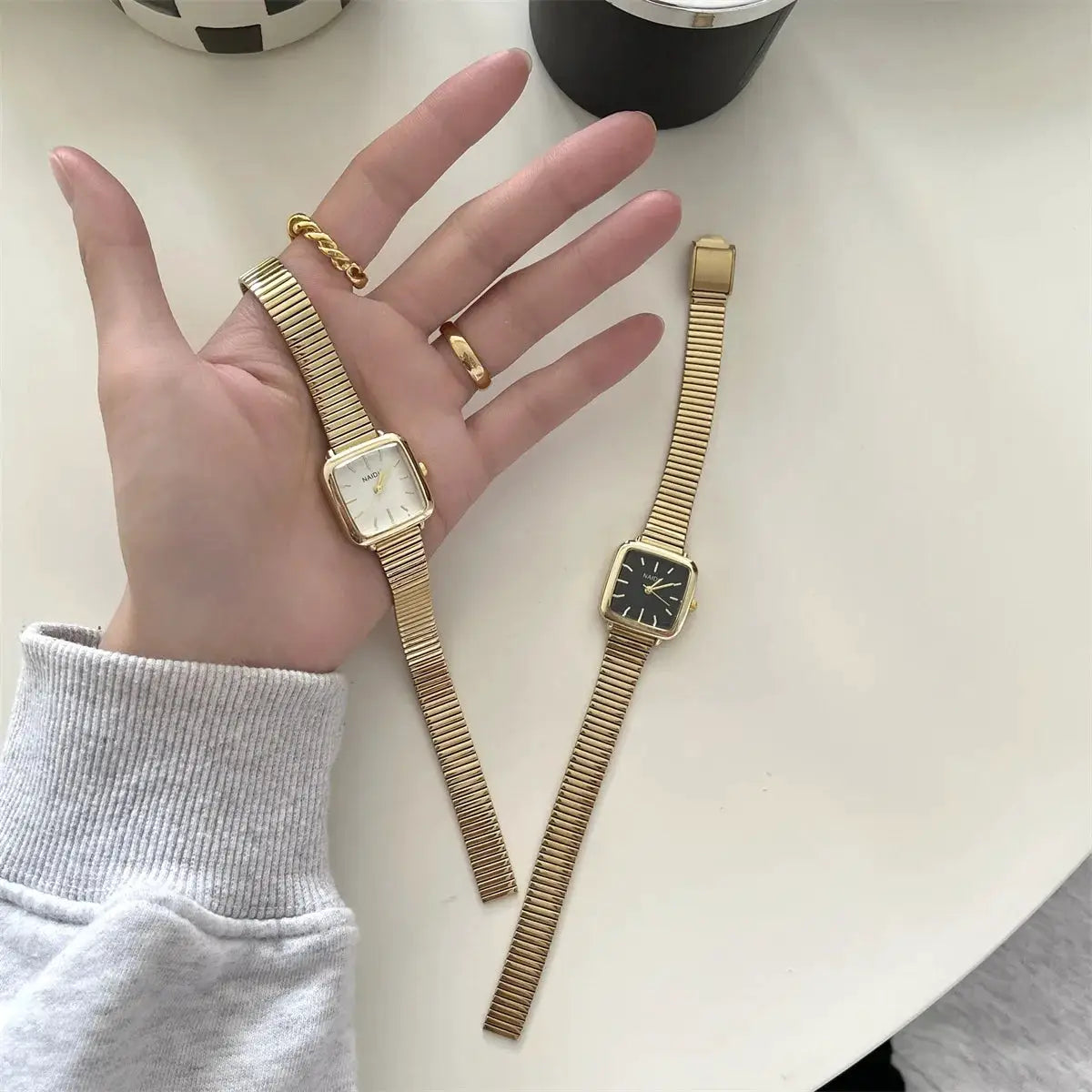 Two gold-tone women's quartz wristwatches with rectangular small dials and adjustable stainless steel bands
