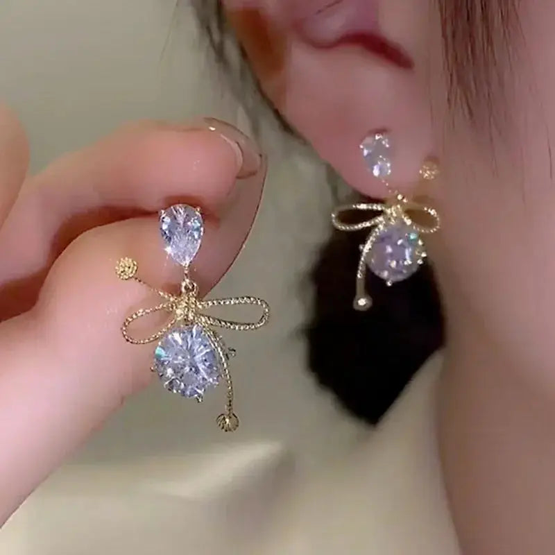 Gold-tone Simples Market earrings with clear crystal drops and bow accents (pair).