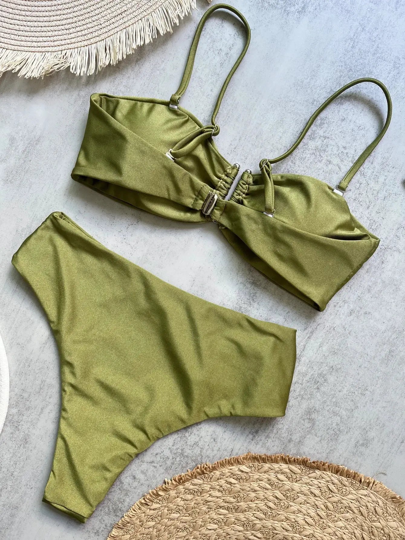 Bandeau bikini set in olive green with ruched top and high-waisted bottoms on a textured surface with a straw mat