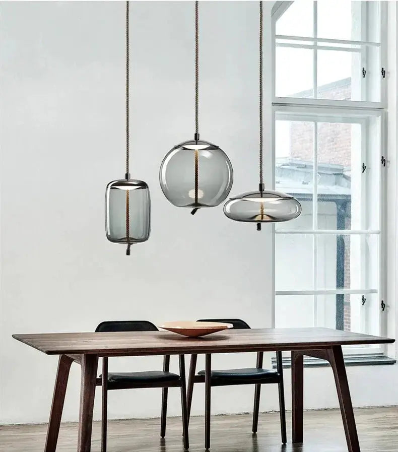 Three glass pendant lamps with hemp-rope suspensions in blue-gray tones above a wooden dining table.