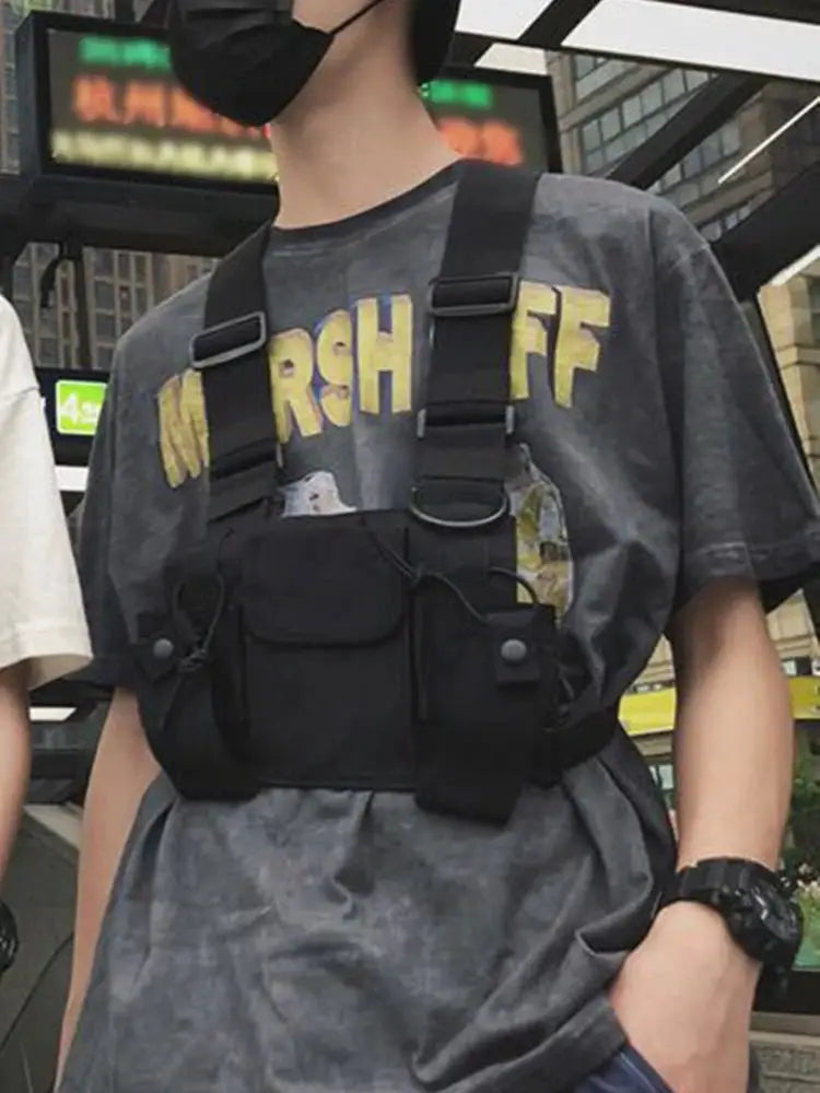 Black tactical chest rig bag with multiple pockets and adjustable straps worn over a gray graphic tee