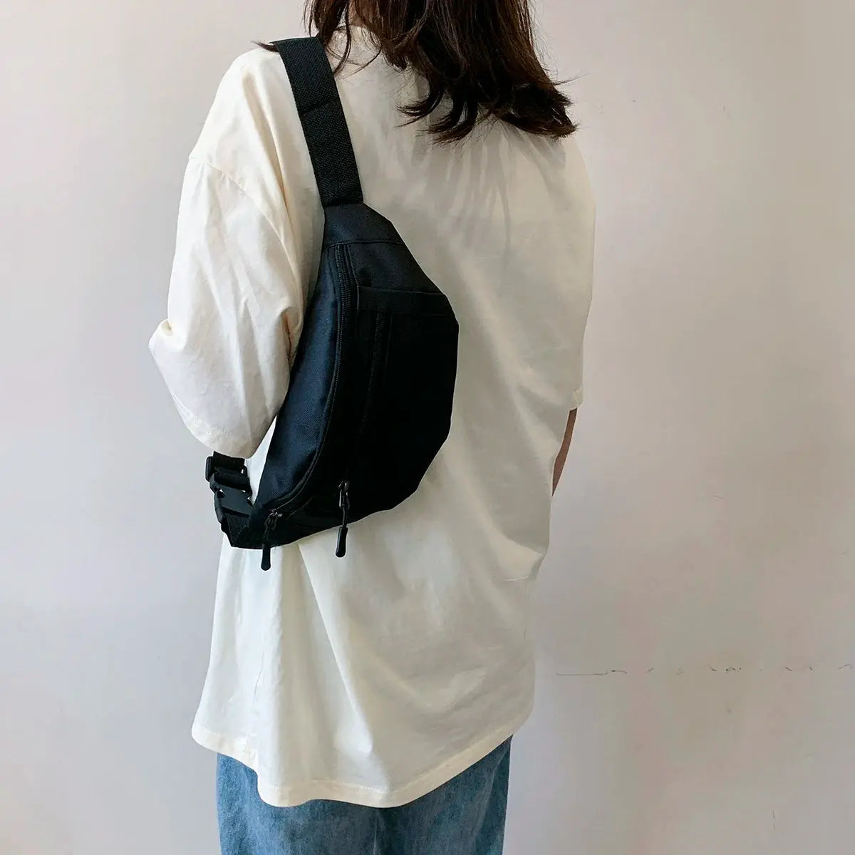 Fanny pack waist bag in black nylon with zippered pockets, worn crossbody.