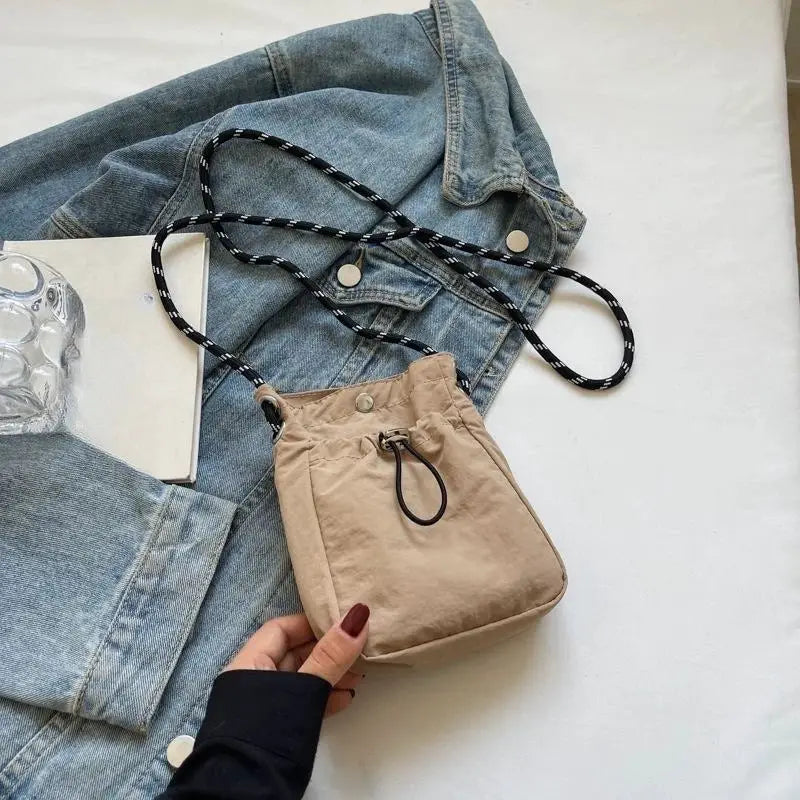Nylon crossbody bag beige compact square purse with a black-and-white braided strap and front drawstring closure.