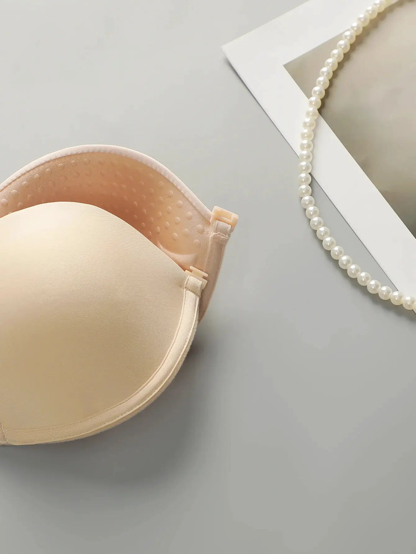 Backless front-closure push-up bra, beige; smooth cups; adjustable straps; pearl necklace beside