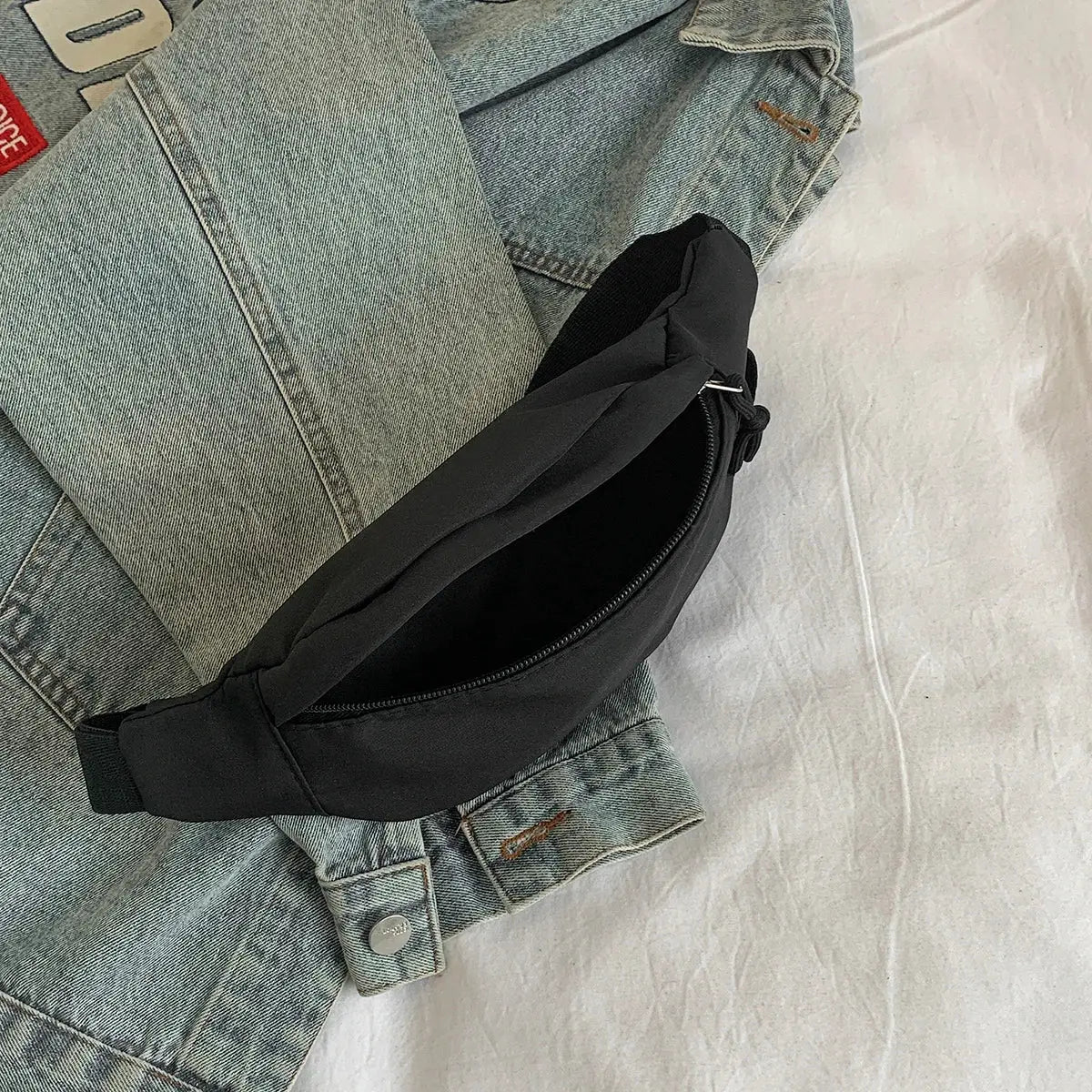 1 black waist bag with zipper, Simples Market, worn around the waist over a blue denim jacket.