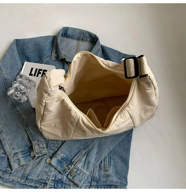 Beige soft-cloth shoulder bag with buckle strap, placed on a denim jacket.