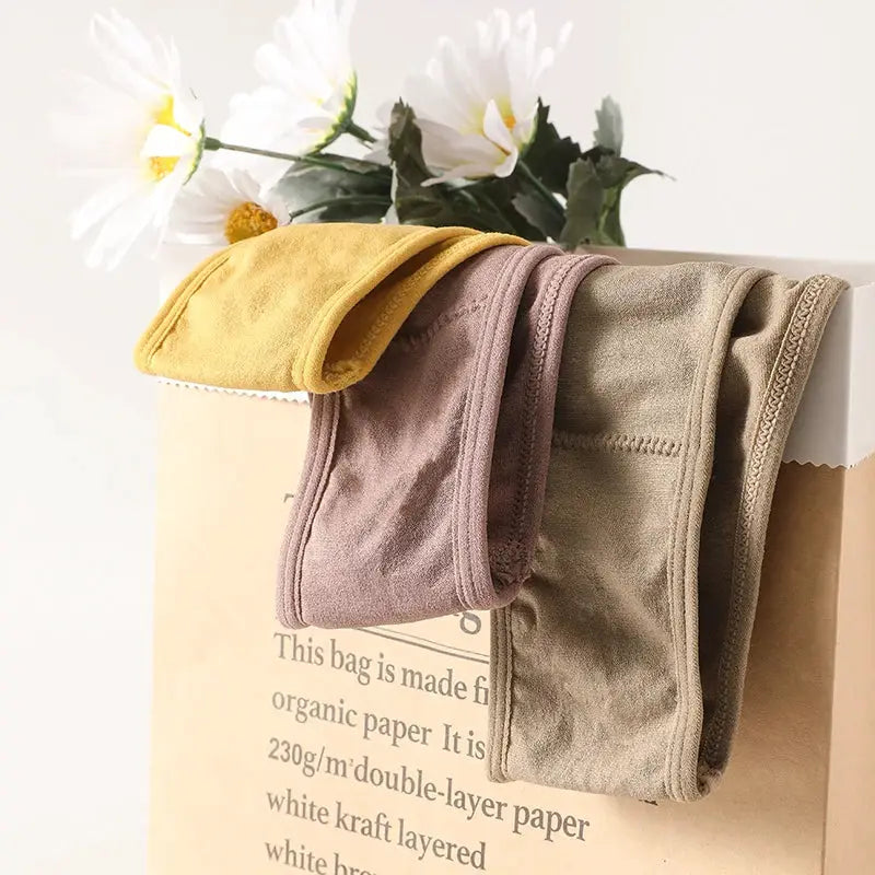 Simples Market women's ribbed low-rise panties, three colors mustard, mauve and taupe, hanging over a bag.