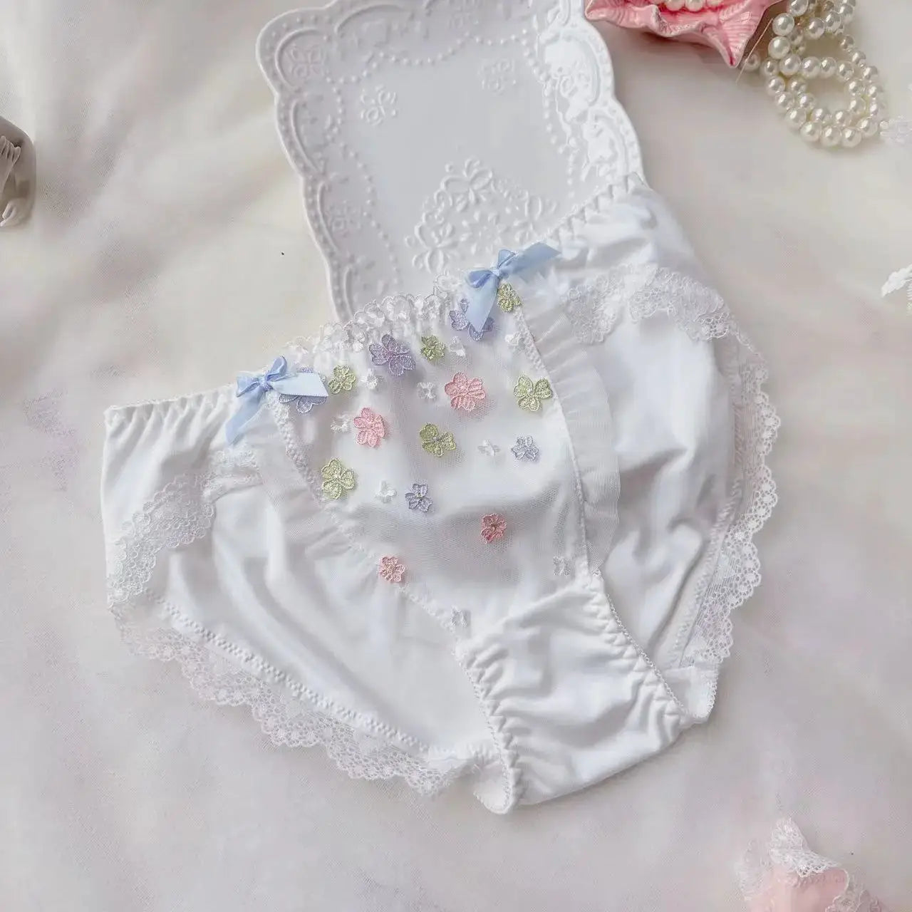 White cotton panties with scalloped lace trim, pastel flower embroidery and blue bow accents.
