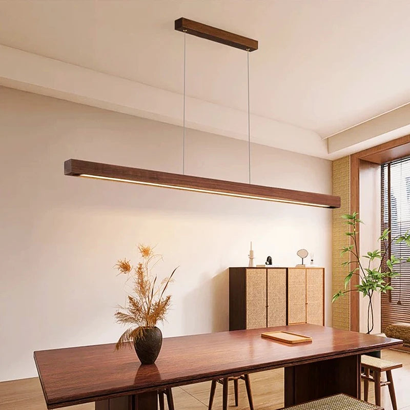 Wooden LED pendant light, long brown strip with dual suspension over a dining table.
