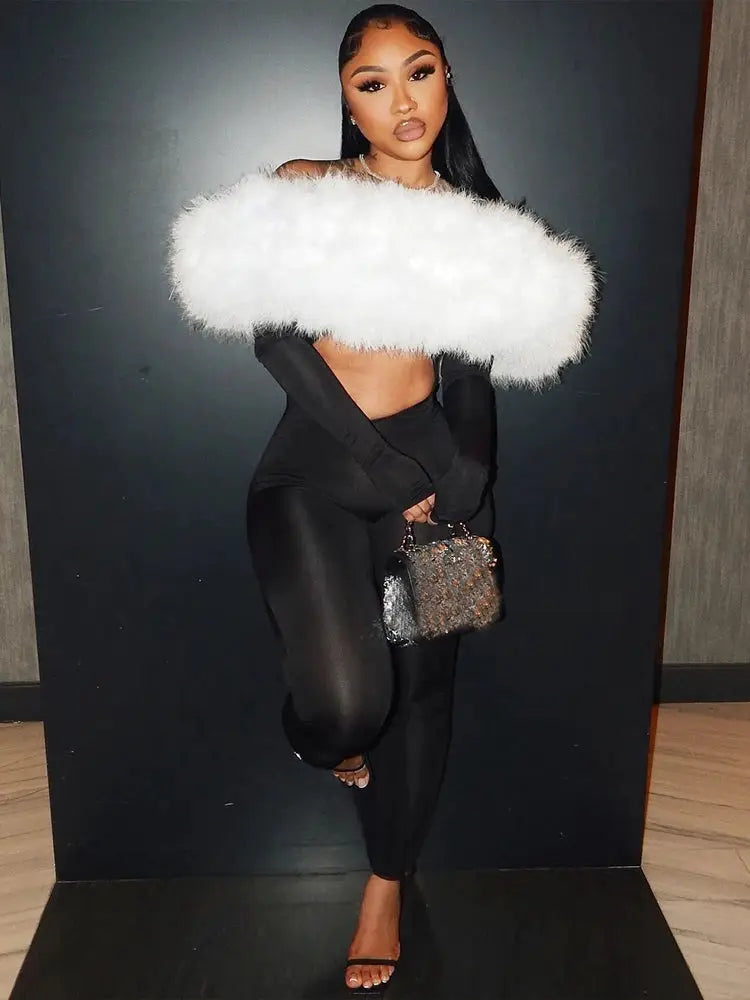 Sisterlinda furry slash-neck jumpsuit in black stretch fabric with white fluffy neckline; model with sparkly handbag