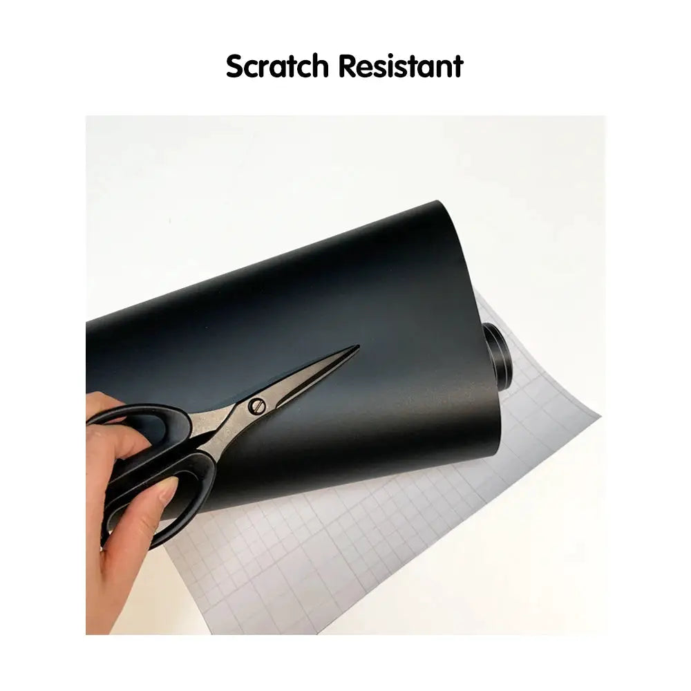 PVC car vinyl wrap sheet in matte black, waterproof decorative film being cut with scissors.