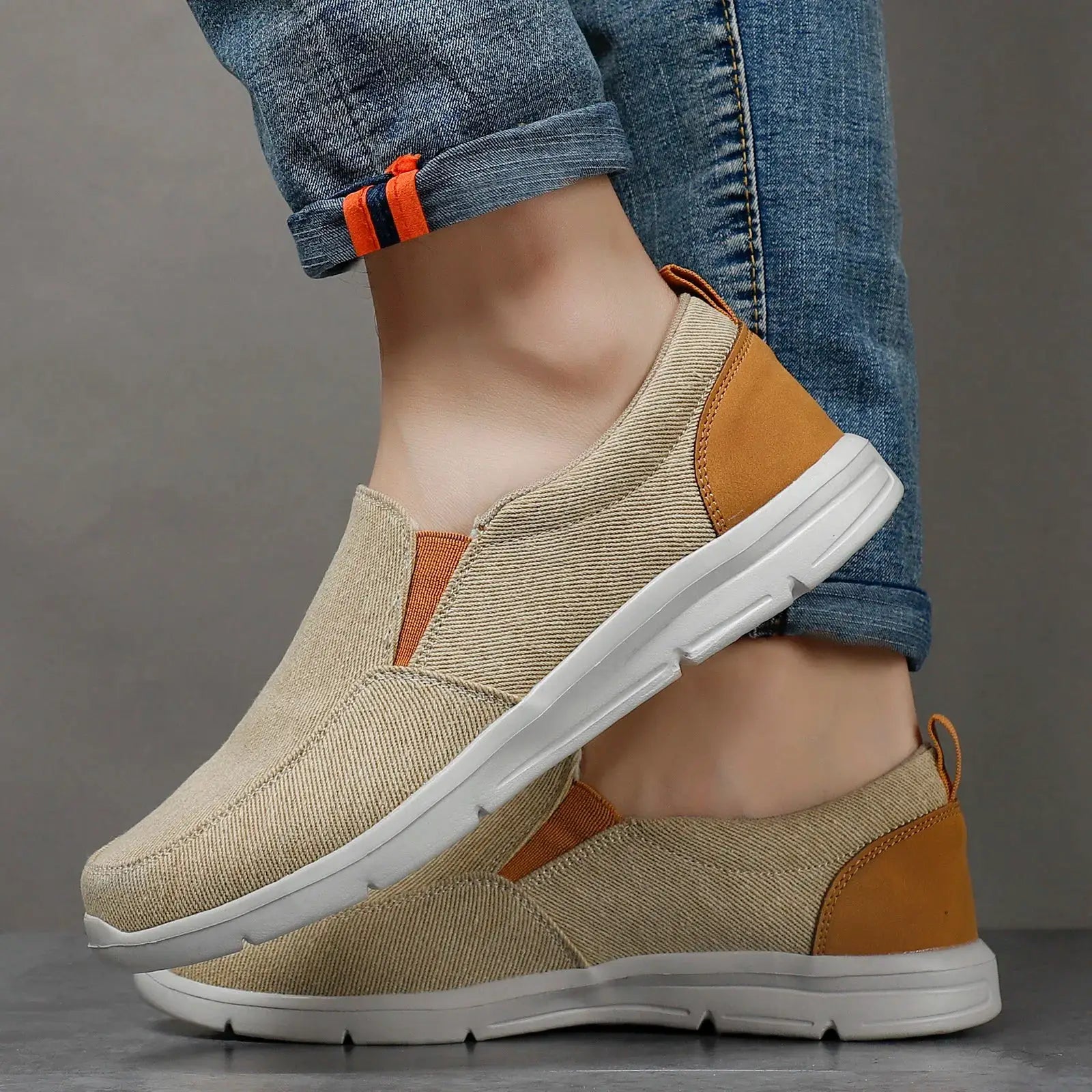 Men's canvas slip-on sneakers in beige with orange heel panel and white sole.