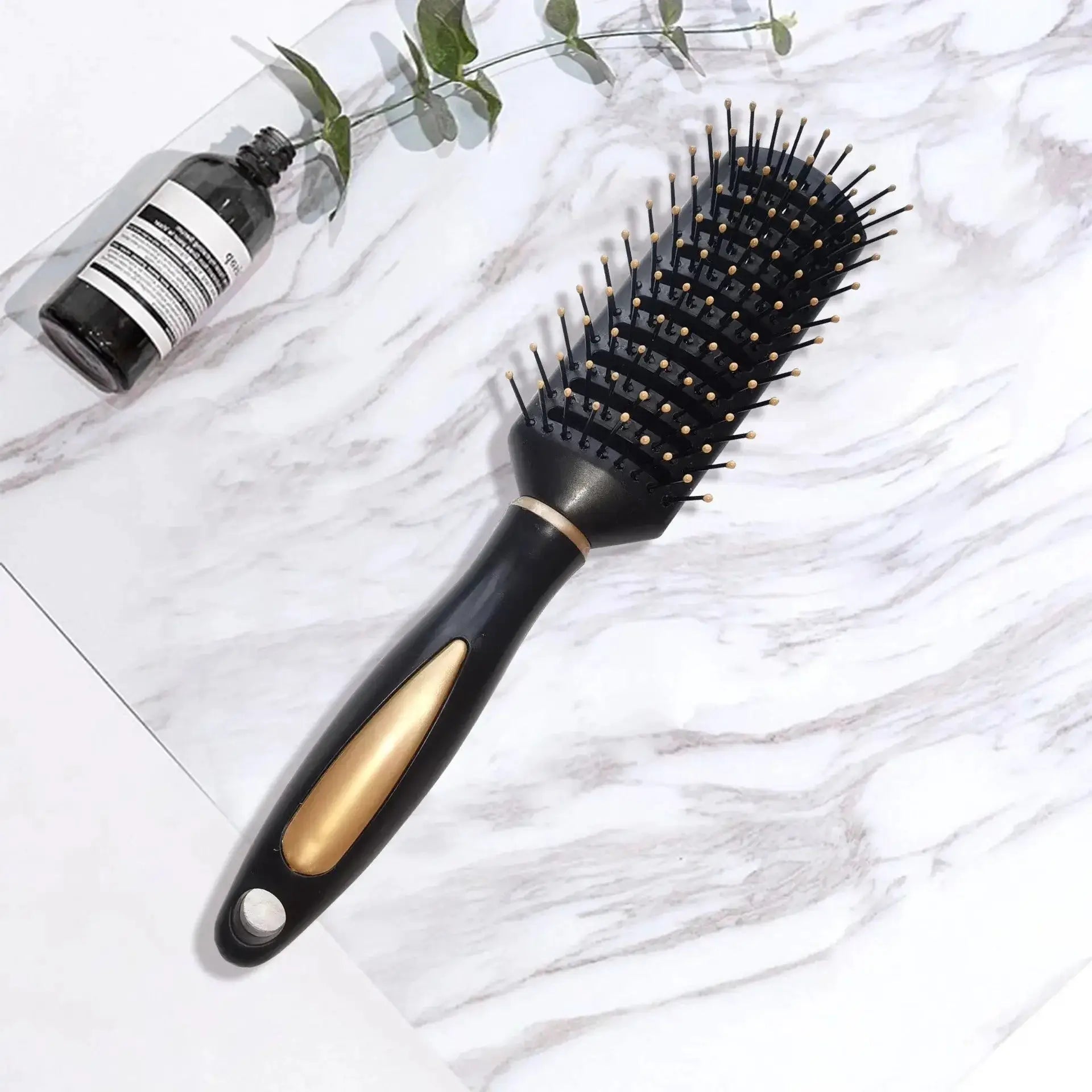 Air bag anti-static hair brush with black plastic handle and gold-tipped bristles, placed beside a bottle on marble surface.