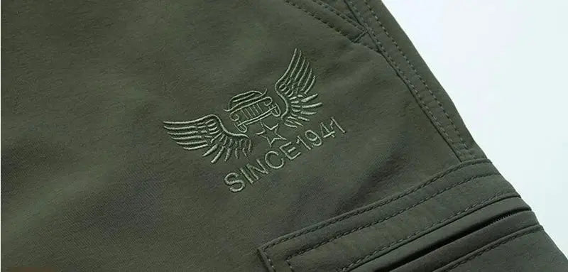 Olive green fleece-lined outdoor work pants with cargo pockets and embroidered winged logo.
