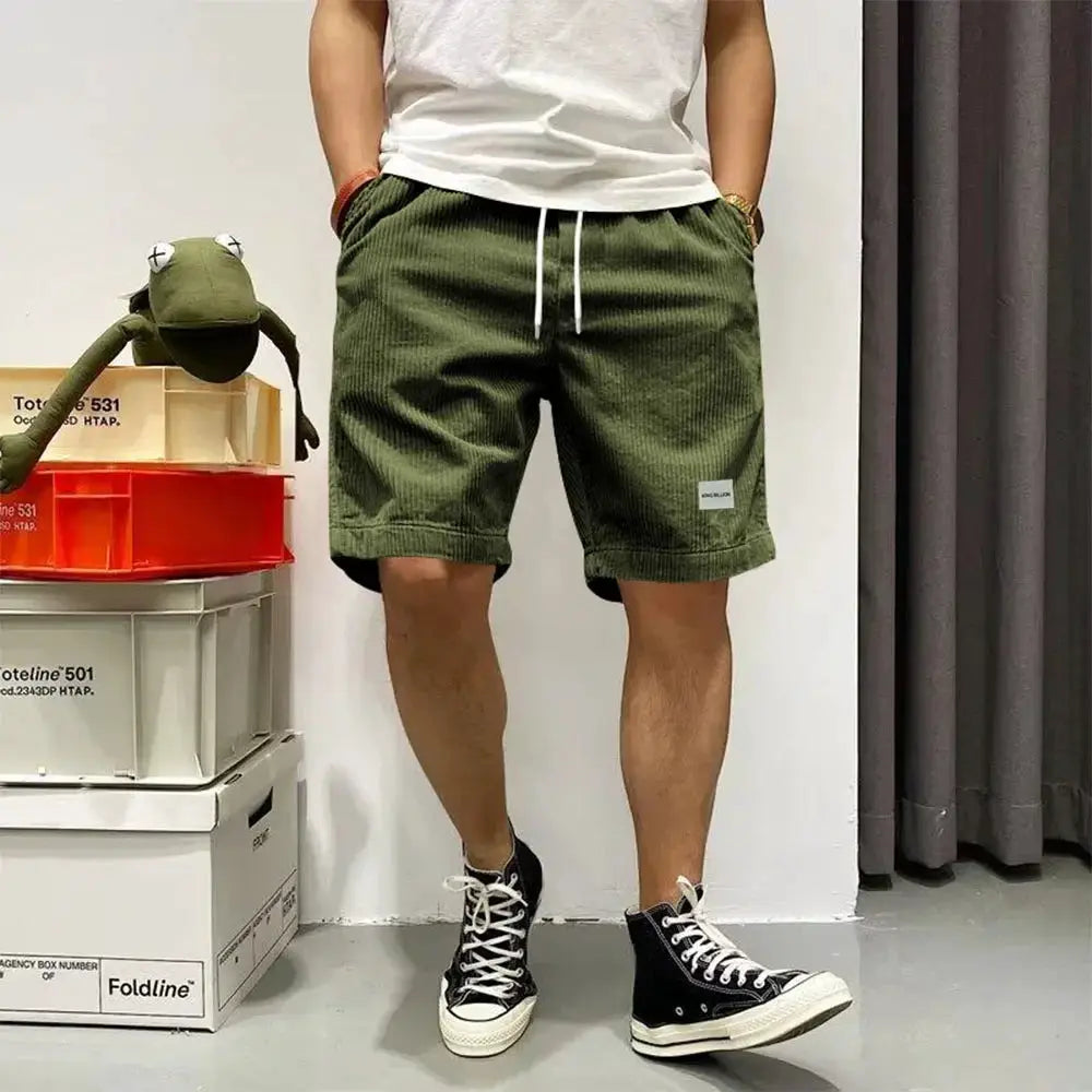 Men's olive green corduroy shorts with elastic waist and white drawstring, baggy basketball-style fit.