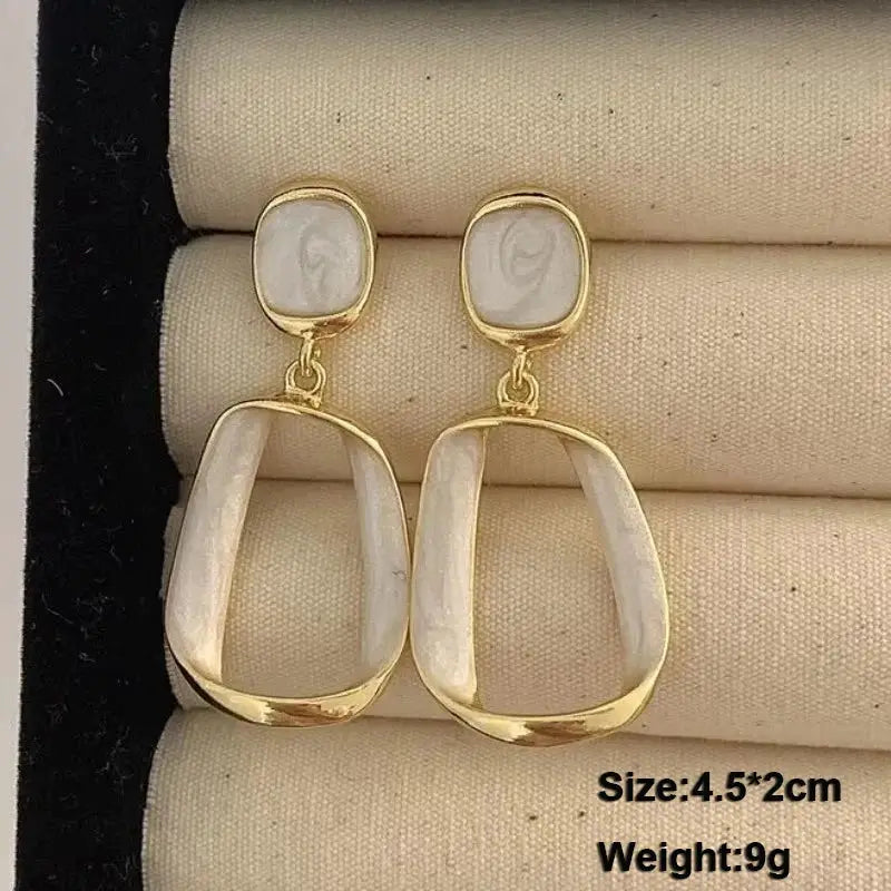 Gold-tone dangle earrings with white acrylic stones; open oval drop design, pair