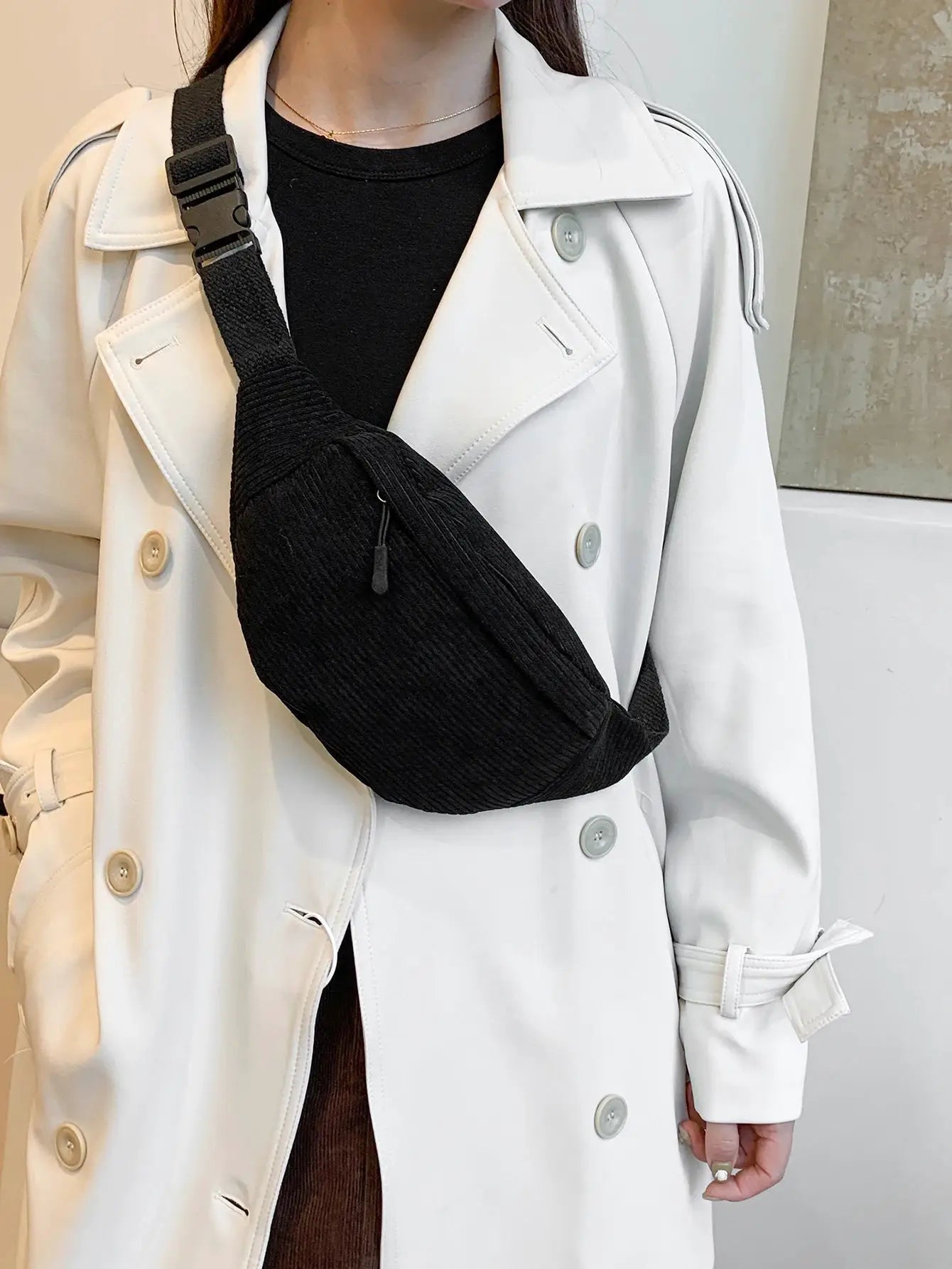 Fanny pack, black ribbed fabric, worn crossbody across the chest over a white trench coat.