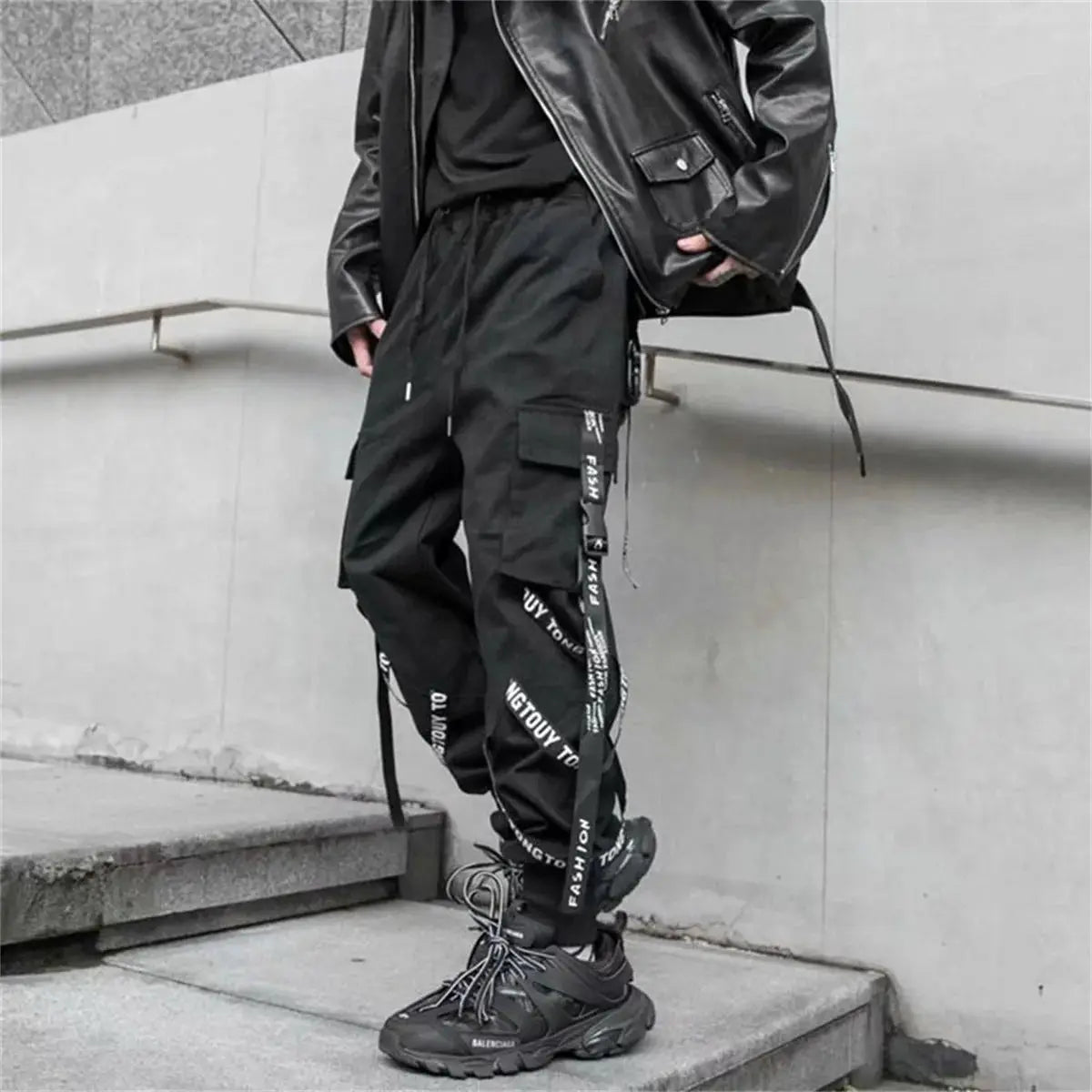Black cargo pants with multiple pockets and strap details, worn with Balenciaga sneakers