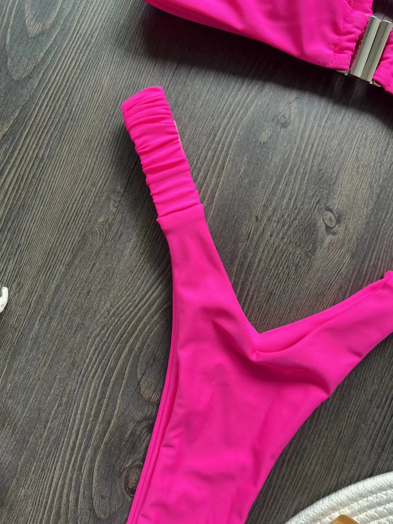 Hot pink micro bikini set with ruched sleeve detail on a dark wood floor