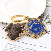 Gold-tone chocolate frog keychain with two charms: a brown frog pendant and a blue ornate square enamel charm.