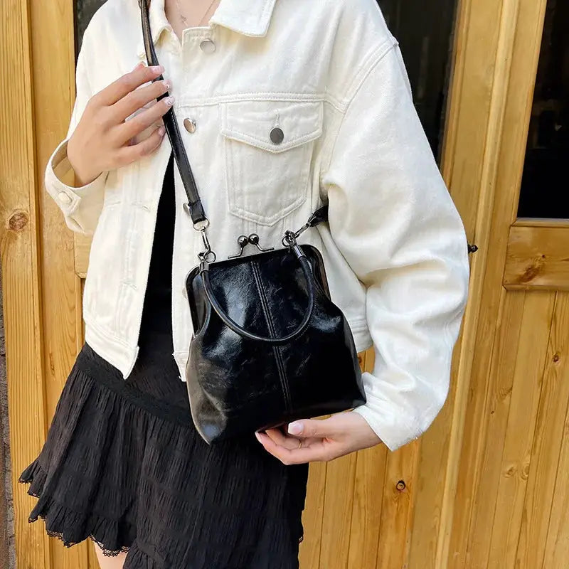 Black PU leather shoulder bag with top handles and crossbody strap, carried by a model in a white denim jacket.