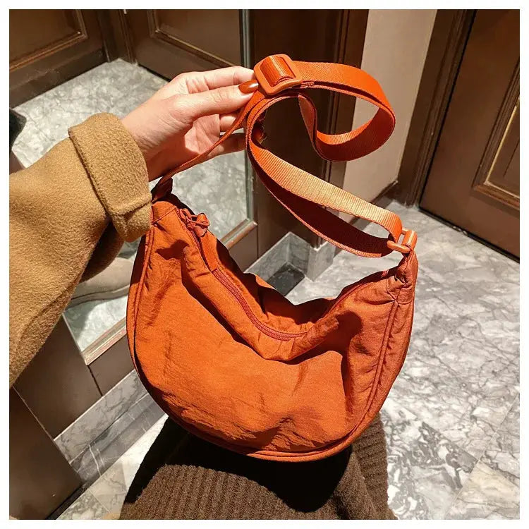 Casual nylon hobo crossbody bag in orange with a wide adjustable strap and zip-top opening.