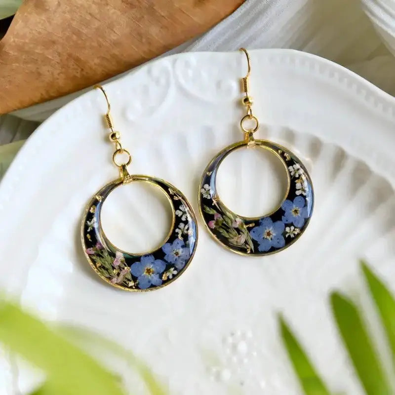 Pressed flower epoxy hoop earrings in blue floral design with gold-tone rim and hooks