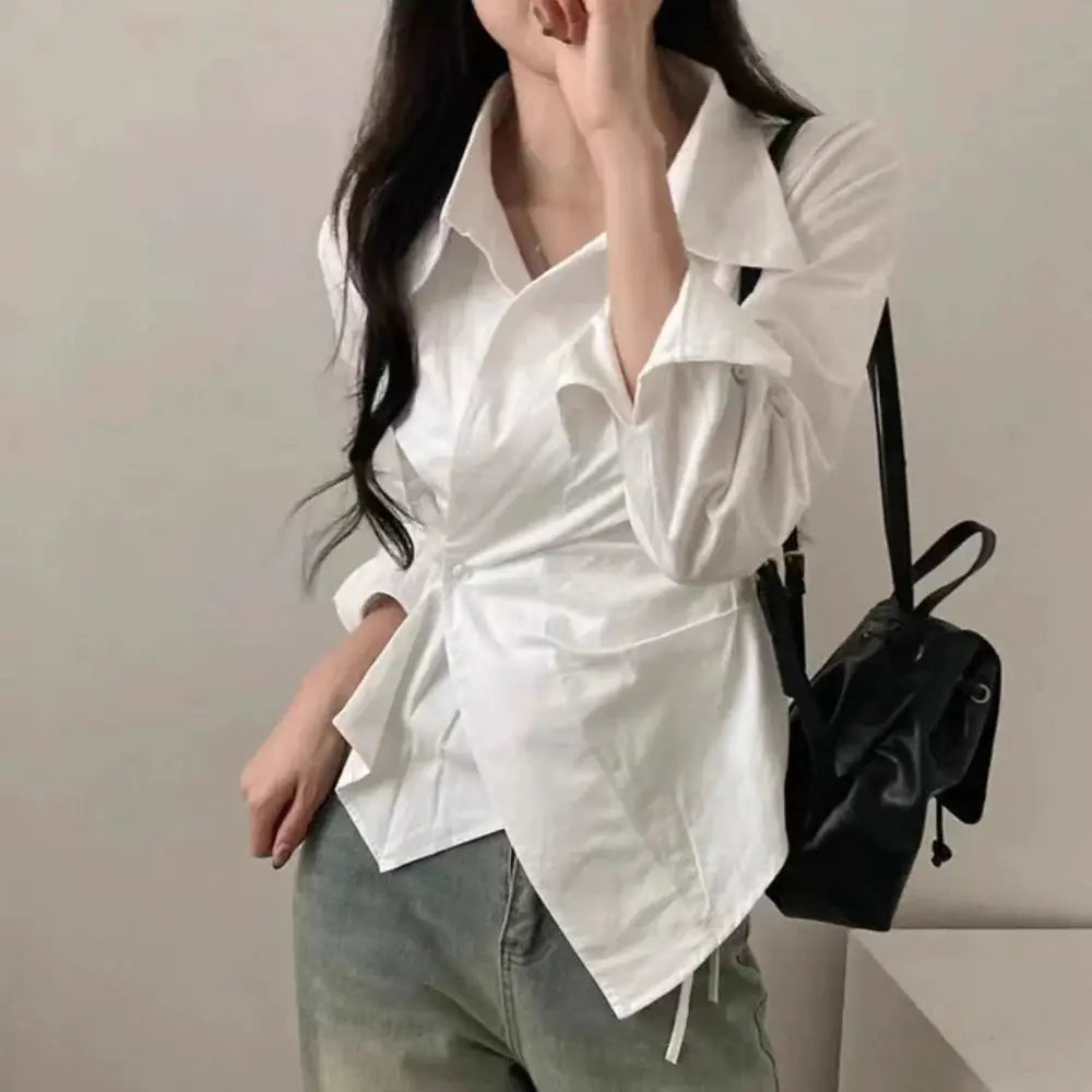 White long-sleeve wrap blouse with collar and waist tie, casual office-ready top paired with jeans and a black backpack.