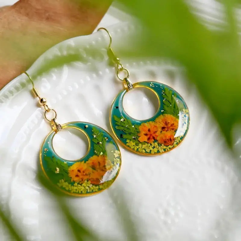 Pair of teal floral epoxy resin earrings with orange pressed flowers and gold-tone hoops.