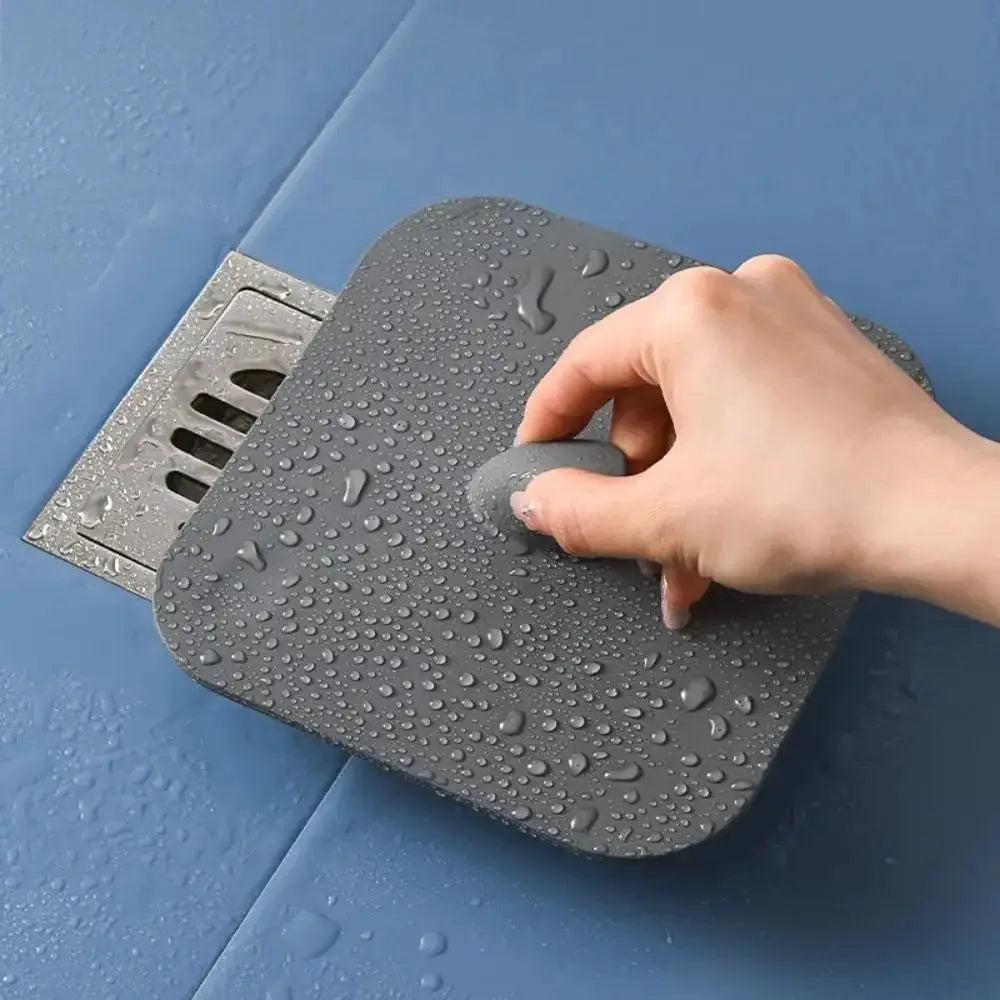 Silicone bathroom floor drain deodorant pad in gray; hand pressing onto drain, water droplets on surface.