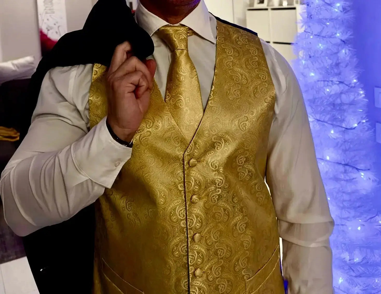 Men's gold paisley jacquard waistcoat and necktie set over white dress shirt; black suit jacket draped over shoulder.