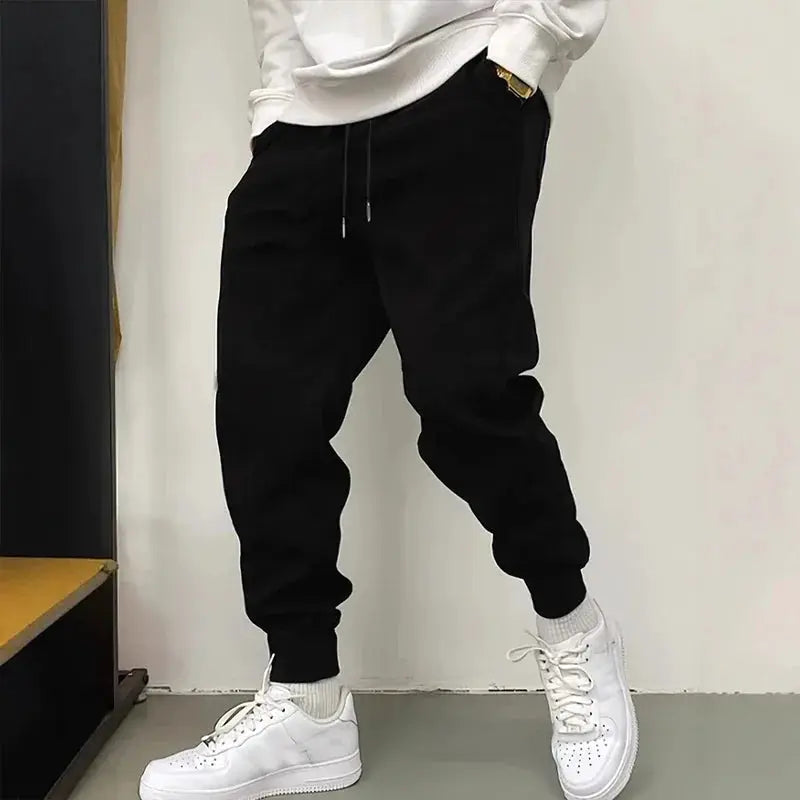Men's black jogger pants with drawstring waist and cuffed ankles, paired with white sneakers