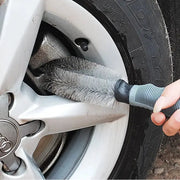 Car wheel cleaning brush with gray bristles and blue-gray handle cleaning an Audi alloy wheel.