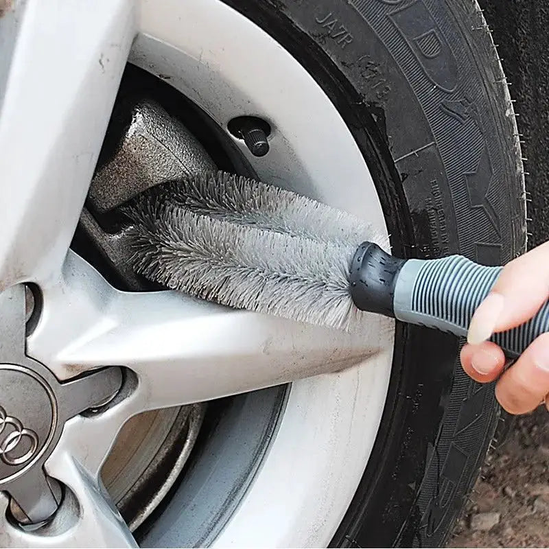 Car wheel cleaning brush with gray bristles and blue-gray handle cleaning an Audi alloy wheel.