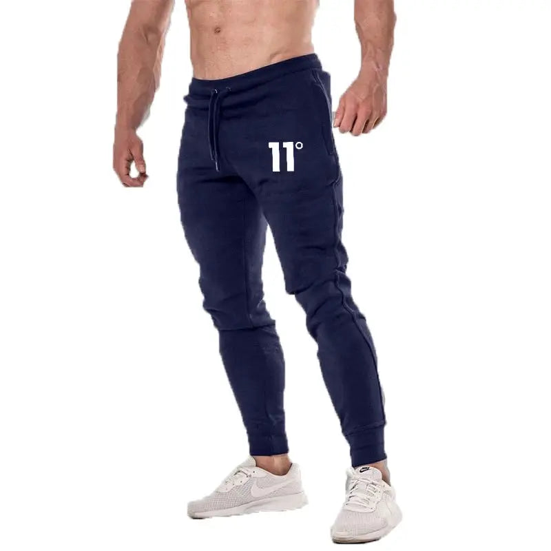 Men's navy joggers with 11° logo, drawstring waist and tapered cuffs, shown with white sneakers.