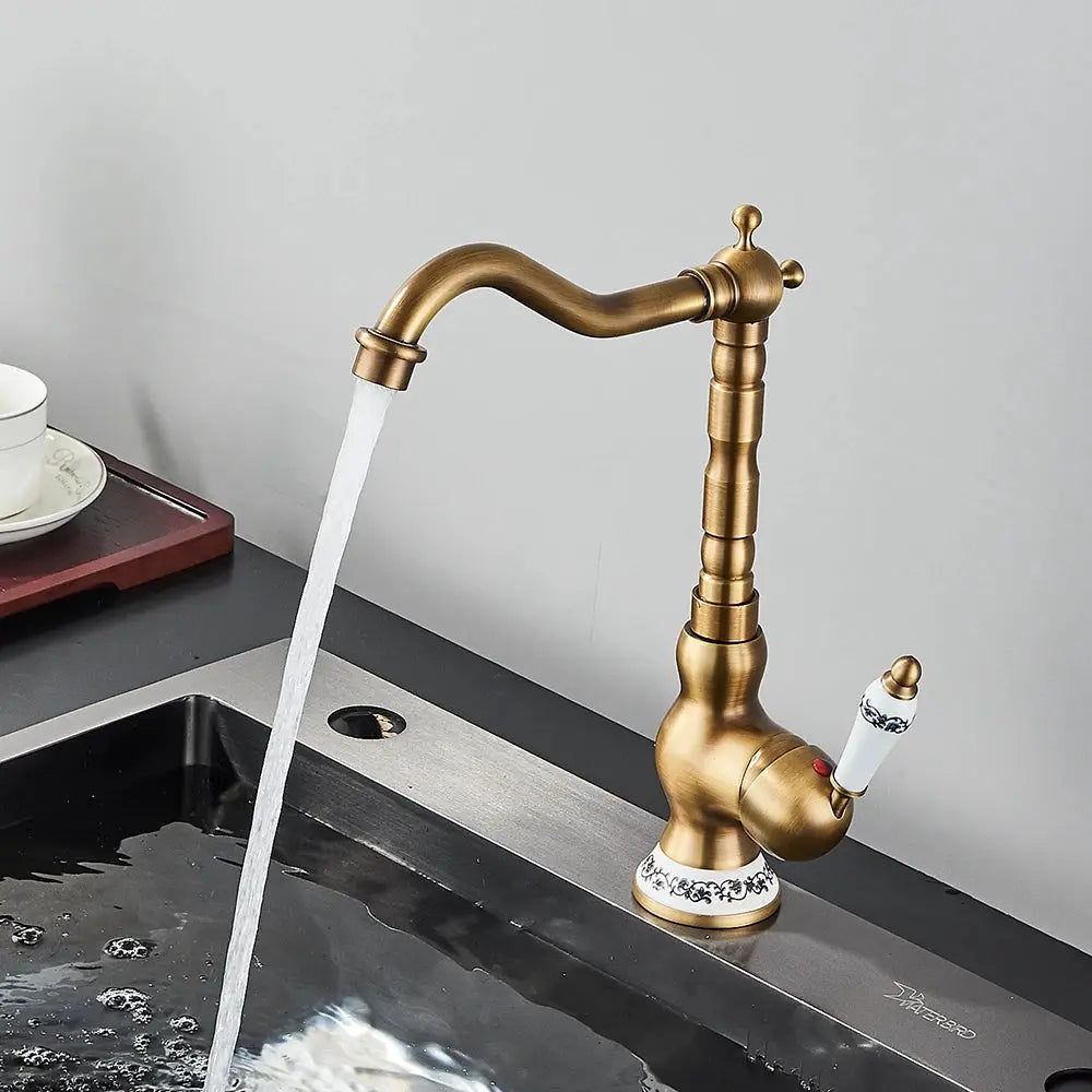 Antique brass bathroom faucet by Simples Market with rotating spout and ceramic patterned handle.